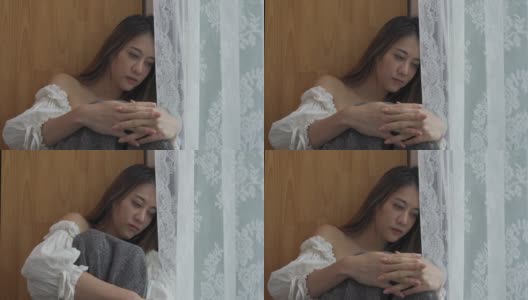 4K沮丧美丽的亚洲女人独自坐在公寓房间的窗户边哭泣和尖叫。孤独悲伤的女孩，想起悲伤烦恼。消极情绪与心理健康的概念。高清在线视频素材下载