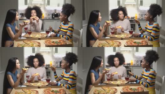 快乐的三名多民族的年轻女子坐在厨房里，吃着披萨，喝着葡萄酒，讲着笑话，放声大笑高清在线视频素材下载