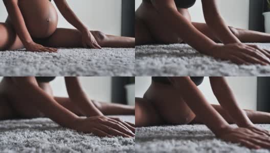 一个大肚子的女人坐在家里的地毯上做伸展运动。高清在线视频素材下载
