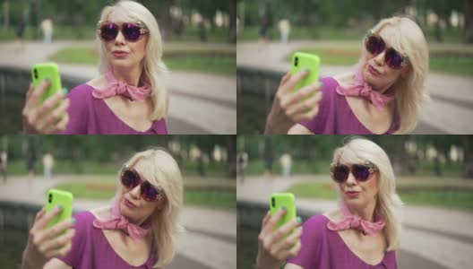 自信的成年女性戴着太阳镜，用智能手机自拍，休息在夏季公园户外。骄傲优雅苗条的白种人女士拍摄周末。休闲的概念高清在线视频素材下载