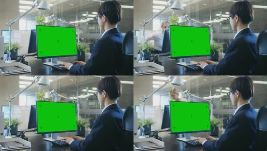 在办公室里，商人在他的办公桌上用一台模拟的绿色屏幕的个人电脑工作。同事走进办公室，并在她的办公桌前发生。高清在线视频素材下载