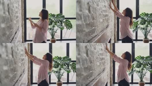 有创意的女人正在装饰她的阁楼风格的公寓，在砖墙上选择美丽的图片和标记点用铅笔。创意和室内概念。高清在线视频素材下载