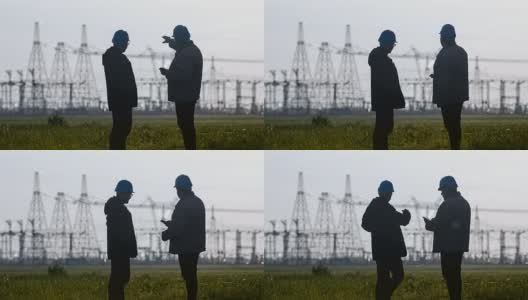 两名工程师戴着安全帽在一个能源站检查期间用智能手机聊天。高清在线视频素材下载