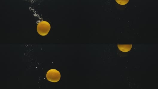 慢动作视频，一个橘子，桔子掉进水在一个黑色的背景高清在线视频素材下载