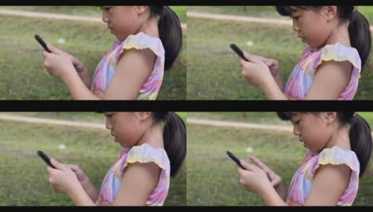 亚洲女孩在绿色公园的户外看智能手机。4k镜头慢动作高清在线视频素材下载