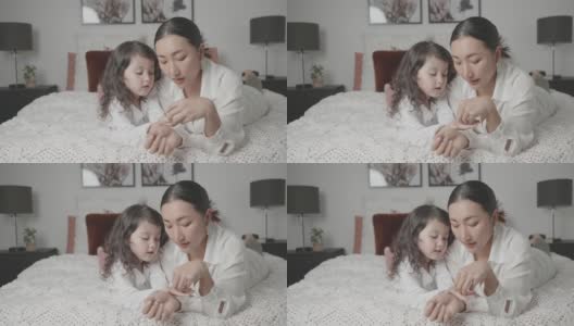 混合亚洲年轻女孩假装玩美甲美容沙龙与她的母亲在床上，家庭生活方式健康的概念高清在线视频素材下载