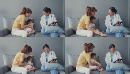 年轻的亚洲女儿科医生和小女孩病人使用数字平板电脑分享良好的健康测试消息与快乐的妈妈坐在沙发在家里。高清在线视频素材下载