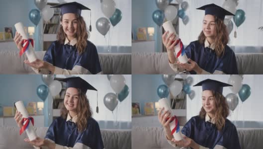 快乐的毕业生肖像，穿着学术袍和帽子，手里拿着文凭，快乐地从大学毕业，坐在沙发背景的气球在大流行期间高清在线视频素材下载