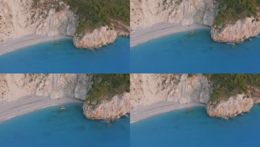 希腊爱奥尼亚岛莱夫卡达美丽的米洛斯海滩的空中倾斜运动。日落时，金色的阳光洒在被蓝绿色大海包围的岩石峭壁上高清在线视频素材下载