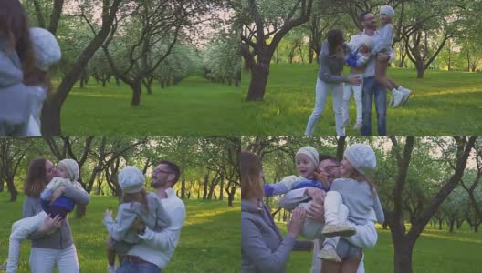 幸福的一家人在草地上拥抱。父母和他们的两个女儿在公园的草坪上拥抱。花期果园。高清在线视频素材下载