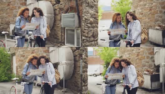 兴奋的年轻女性自行车旅行者看地图，笑着环顾四周，而站在国外的街道上的自行车。人与旅行的概念。高清在线视频素材下载