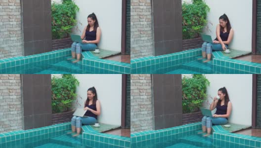 一个穿着休闲服在笔记本电脑上工作的女人，早上坐在游泳池边喝咖啡，把腿放在水里放松在一个豪华度假酒店。概念商务人士在周末活动。高清在线视频素材下载