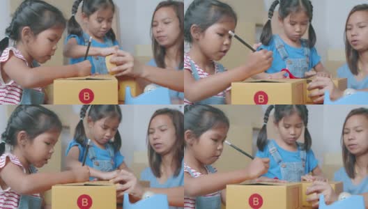两个小女孩帮助家长在盒子里写上地址，用胶带把产品包装好，然后邮寄给在线客户，充满乐趣和快乐。高清在线视频素材下载