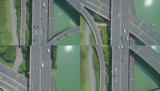 从空中俯瞰高速公路立交桥多层路口，快速移动的汽车被绿树环绕，在阳光明媚的一天，有一条河在一边。高清在线视频素材下载