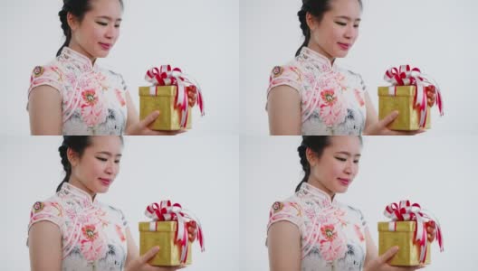 特写:中国/亚洲妇女穿着旗袍白色的衣服打开一个金色的大礼盒，在她的家人，亲戚和朋友的新年快乐，在中国的新年节日高清在线视频素材下载