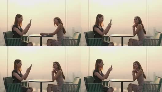 日落时分，4K亚洲女性朋友在屋顶餐厅用智能手机拍照。高清在线视频素材下载