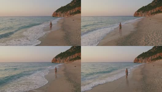 空中低空跟随成年妇女享受美丽的米洛斯海滩的Lefkada，爱奥尼亚岛，希腊。夕阳金色的阳光和原始的海浪打破了蓝绿色的大海在岸边高清在线视频素材下载