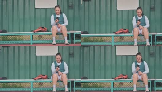 一名亚裔华裔中年女子坐在网球场的长椅上，在比赛结束后用智能手机查看自己的心跳高清在线视频素材下载