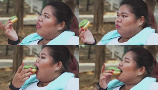 超重的年轻女人在公园吃甜甜圈高清在线视频素材下载
