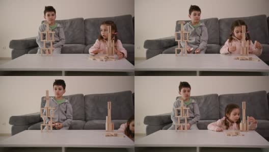 可爱的欧洲孩子一起玩棋盘游戏。一个英俊的学龄男孩，用木砖砌成房子，坐在沙发上，旁边是他的小妹妹，她的塔倒塌了，她很难过高清在线视频素材下载
