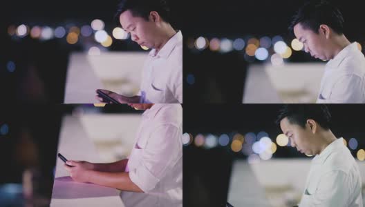 在泰国曼谷的城市夜晚，一个年轻人在摆弄他的手机高清在线视频素材下载