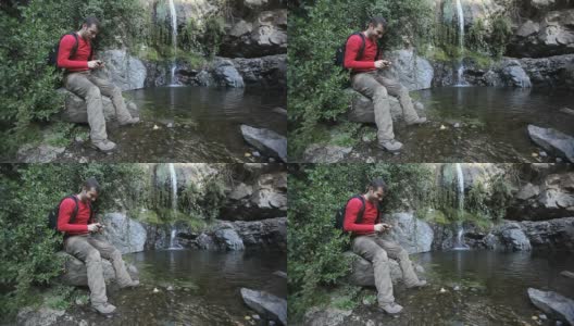 一个年轻人在瀑布前拿着智能手机。高清在线视频素材下载