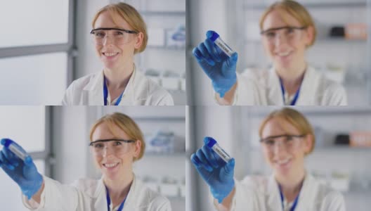 实验室研究人员戴着安全眼镜，面带微笑，手里拿着标有疫苗的试管高清在线视频素材下载