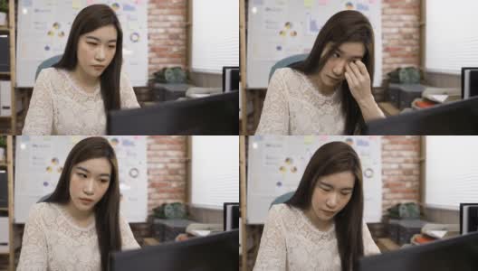 不舒服的亚洲女商人坐在电脑后揉她的眼睛和努力眨眼，试图清楚地看到在办公室的工作。高清在线视频素材下载