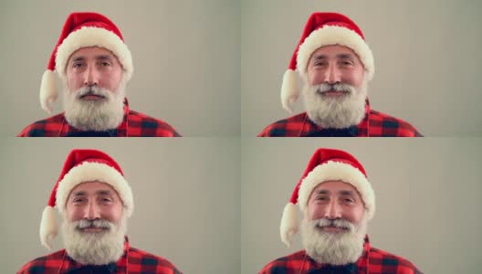 灰色背景上，一位年长的成年人看着镜头，微笑着戴着圣诞老人的帽子。慢动作高清在线视频素材下载
