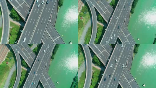 从空中俯瞰高速公路立交桥多层路口，快速移动的汽车被绿树环绕，在阳光明媚的一天，有一条河在一边。高清在线视频素材下载