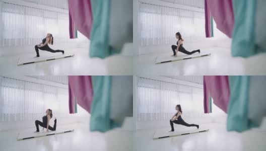 年轻的亚洲妇女训练瑜伽姿势新月形弓步在膝盖上，手放在床垫上。年轻苗条的女孩穿着黑色运动服，在健身室的白色床垫上做有氧伸展运动，舒缓肌肉紧张，增强柔韧性高清在线视频素材下载