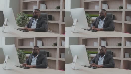 非洲裔美国男性商人在办公室工作期间使用电脑打字。成年的公司老板坐在办公桌前。现代成功人士的概念。商业领导与管理理念高清在线视频素材下载