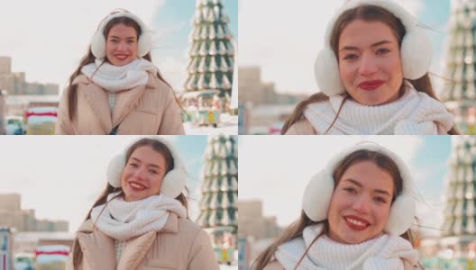 年轻女子穿着毛皮耳套和白色针织围巾站在冬季户外城市街道上，背景是圣诞树高清在线视频素材下载