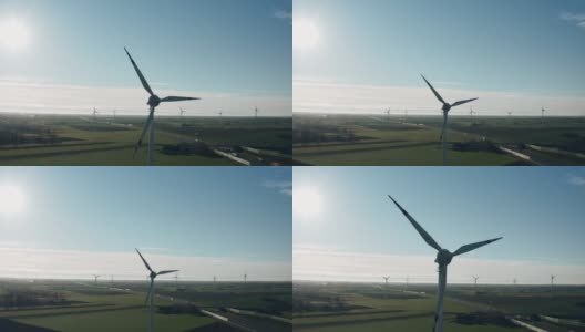 在阳光明媚的秋日，无人机看到风力涡轮机在绿色的农田里通过公路产生清洁的生态电力。风力发电场生产替代绿色可再生能源高清在线视频素材下载