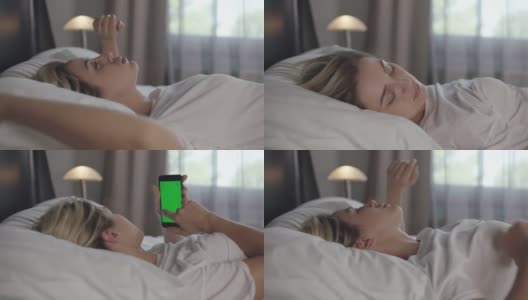 一名年轻女子在家中的床上躺着一部绿色屏幕的手机。高清在线视频素材下载