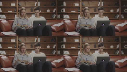 两个20多岁的学生在写文章，女性在书上听写信息，男性在笔记本电脑上打字。学生们在沙发上进行团队合作。高清在线视频素材下载