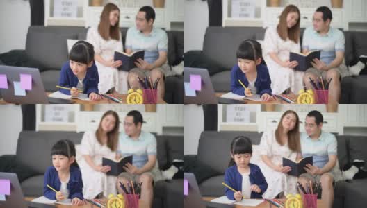 亚洲快乐的女儿正在使用笔记本电脑通过互联网学习，而父母坐在家里的沙发上。电子学习的概念高清在线视频素材下载