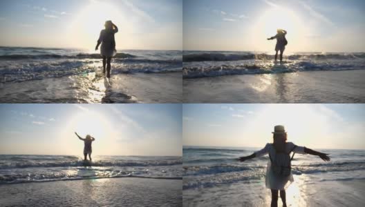 年轻快乐的女人穿着衬衫和背包跑到海边，用她的脚泼水在日出。漂亮的女孩戴着帽子享受暑假或假期。旅行的概念。后视图慢动作高清在线视频素材下载