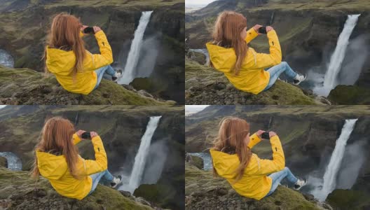 一名女子坐在峡谷边缘，拍摄瀑布的照片高清在线视频素材下载