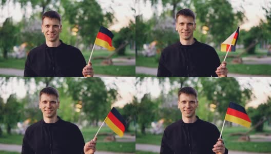 慢动作肖像欢快的德国球迷挥舞官方旗帜，看着镜头，而站在伟大的现代公园美丽的树木和草坪。高清在线视频素材下载