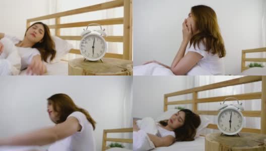 年轻美丽的亚洲女人醒来和伸展在她的床在家里，闹钟醒来的概念高清在线视频素材下载