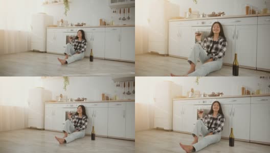 幸福的家庭的主人。年轻开朗的亚洲女人坐在厨房地板上，喝着葡萄酒，享受着她自己的公寓高清在线视频素材下载