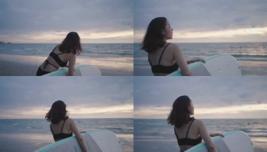 亚洲妇女持有一个sup板和划桨和行走在海滩上。背景是大海和日落。后视图。夏天冲浪。高清在线视频素材下载