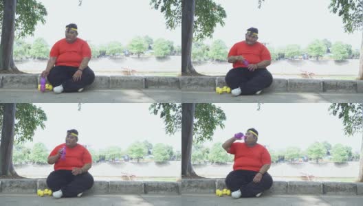 一个肥胖男子坐在公园里喝水高清在线视频素材下载