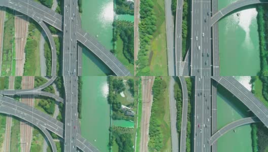 从空中俯瞰高速公路立交桥多层路口，快速移动的汽车被绿树环绕，在阳光明媚的一天，有一条河在一边高清在线视频素材下载