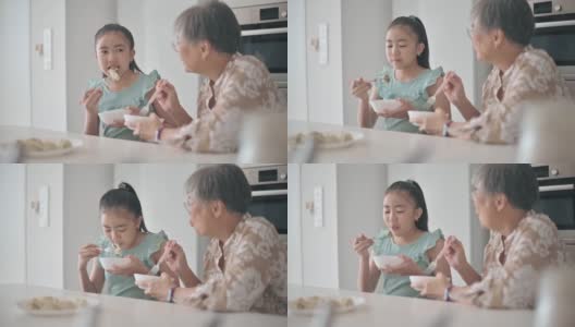 亚裔华人老太太和她的孙女在厨房的柜台上吃饺子高清在线视频素材下载