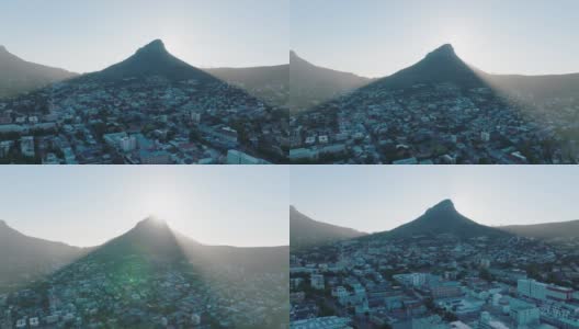 高耸的尖峰在城市的居住区投下阴影。空中上升的镜头显示狮子头山背后的灿烂阳光。南非开普敦高清在线视频素材下载