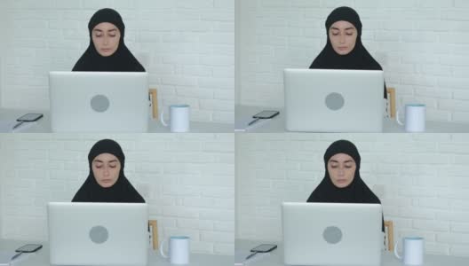 穆斯林女商人在办公室用电脑工作。一名戴着黑色头巾的妇女在阿拉伯世界的金融行业工作，使用笔记本电脑、智能手机以及其他技术高清在线视频素材下载