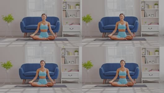 平静的健康亚洲年轻女性坐在地毯上呼吸瑜伽莲花姿势，瑜伽冥想年轻健康女性放松和舒适的白色舒适的家，瑜伽锻炼为健康的概念高清在线视频素材下载