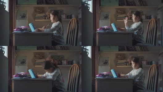 图为，一名小女孩在家中的远程教育教室里，与老师一起用平板电脑进行在线授课，并在书桌上用笔记本书写的真实画面。Covid高清在线视频素材下载